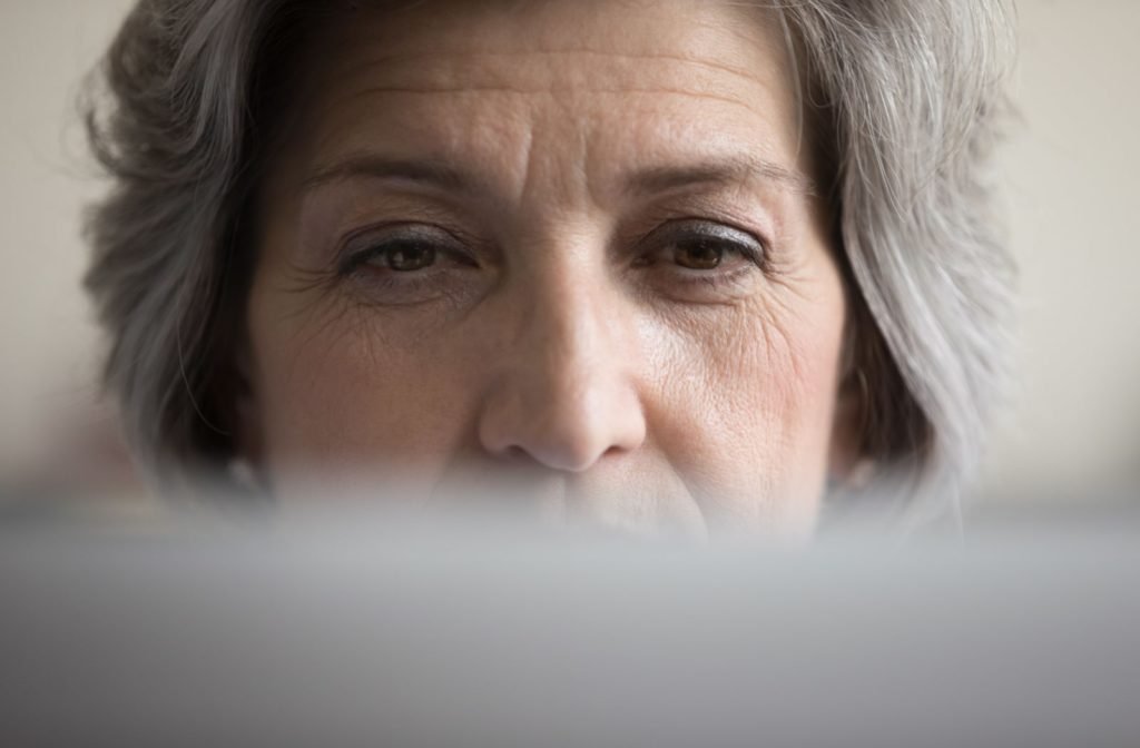 An older woman looking straight ahead at a computer screen, with the screen taking up only a small portion of the bottom of the image.