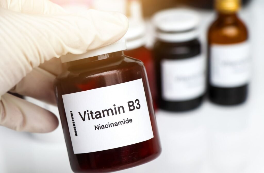 A person wearing rubber gloves and holding onto a bottle of Niacinamide vitamins